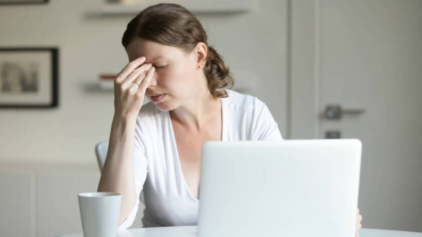 Portrait of a woman on her desk with a laptop, one hand on her forehead.
